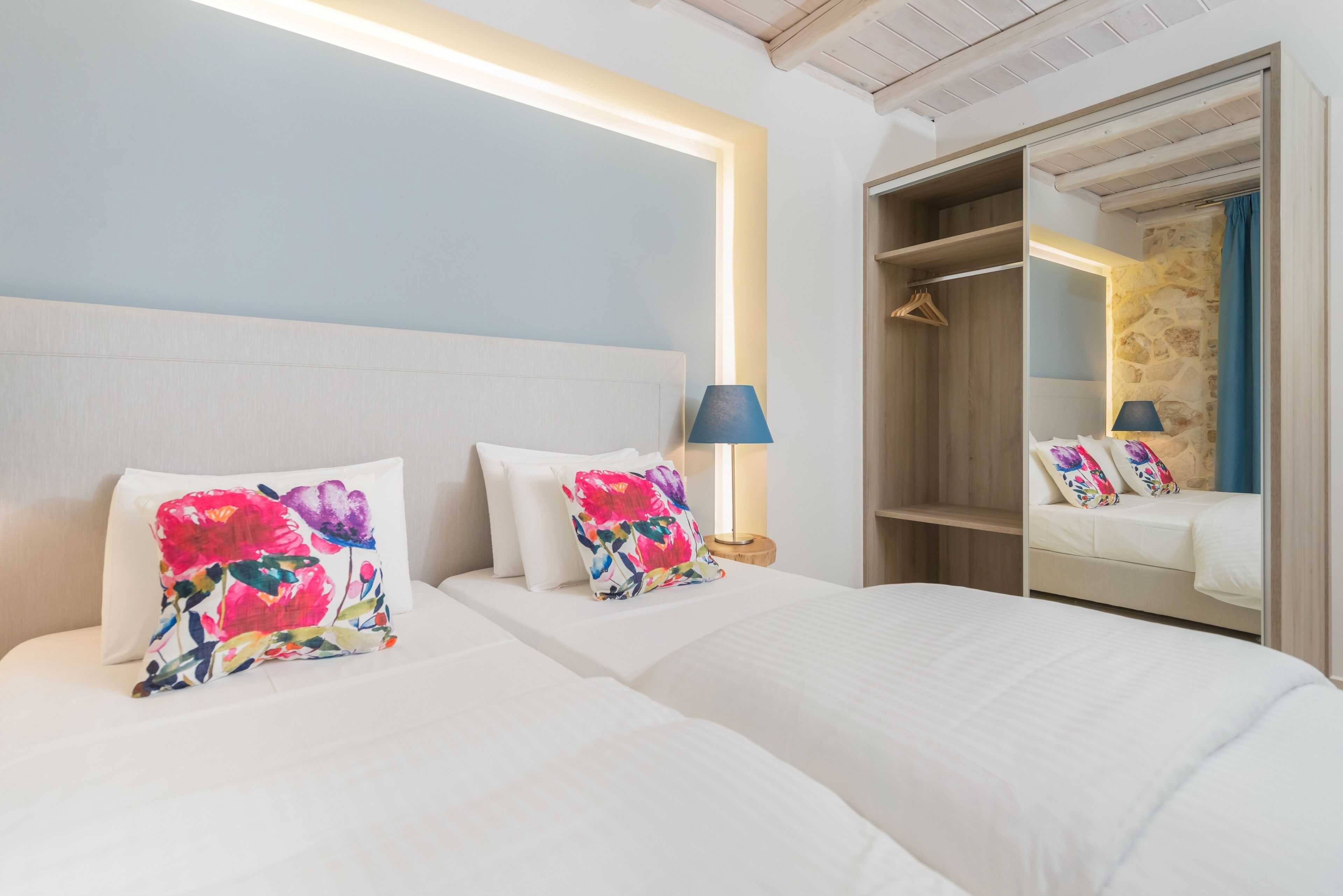A hotel room with two beds, a large mirror, and a wardrobe with a hanging rack.