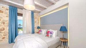 Una camera da letto con parete in pietra, un letto grande con biancheria bianca, due lampade e vista sull'esterno.