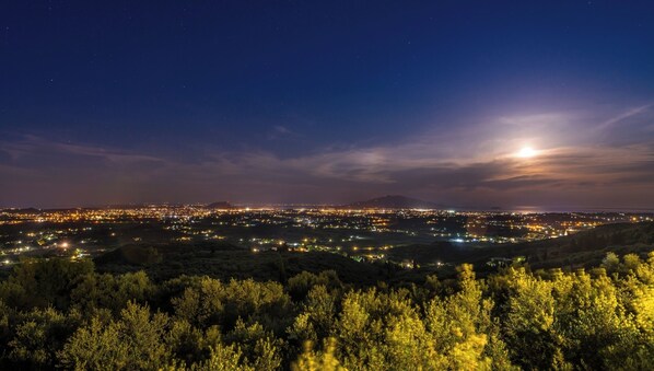 Une vue nocturne d’une ville, avec une colline bien visible au premier plan et une vaste étendue d’eau à l’horizon.
