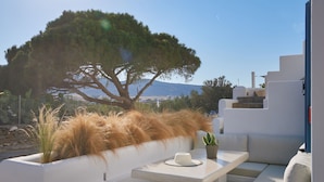 Un área de estar al aire libre moderna con una mesa blanca, una planta en maceta y un gran árbol que da sombra.