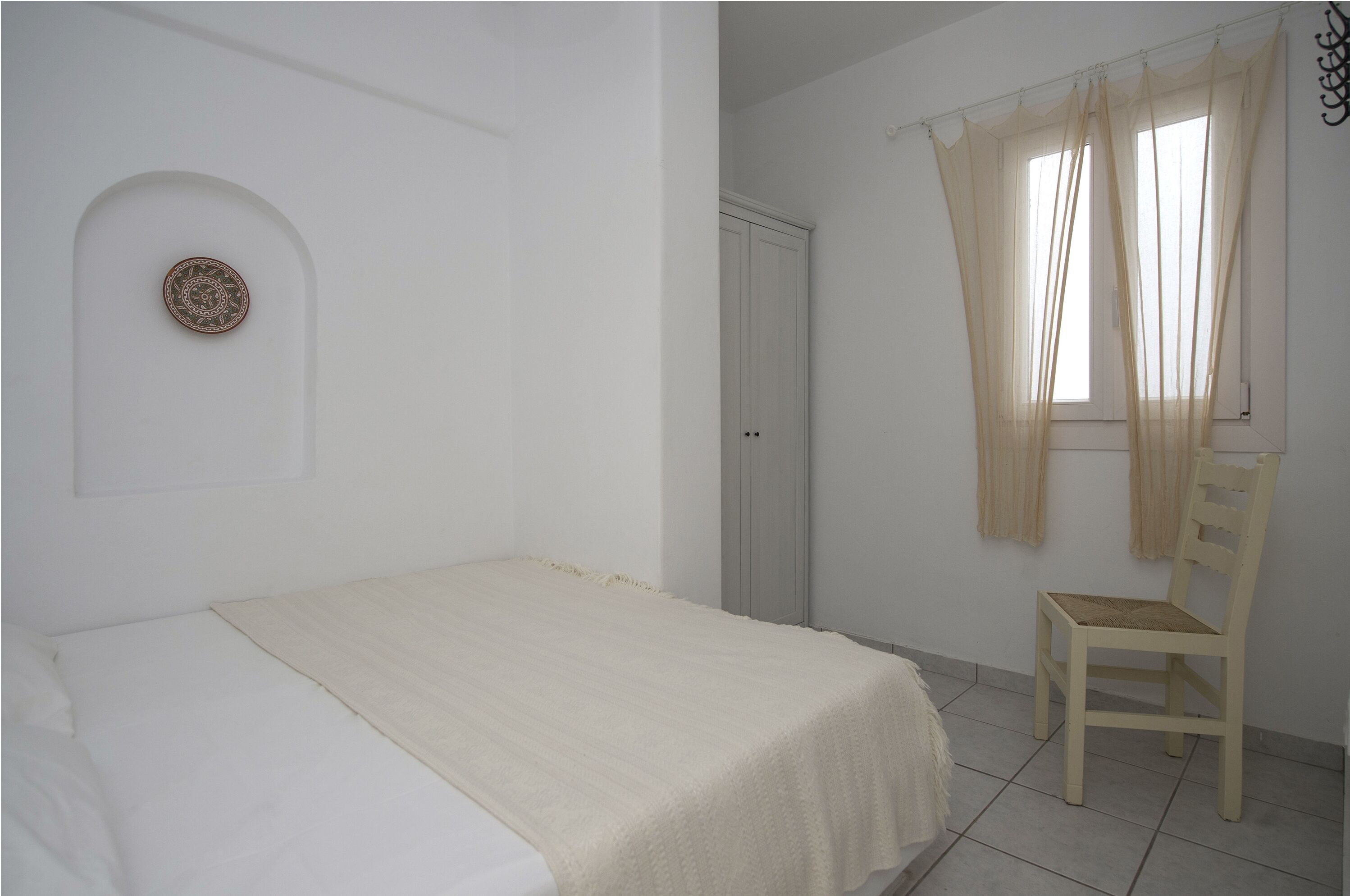A bedroom with a bed, a chair, a wardrobe, and a window with curtains.