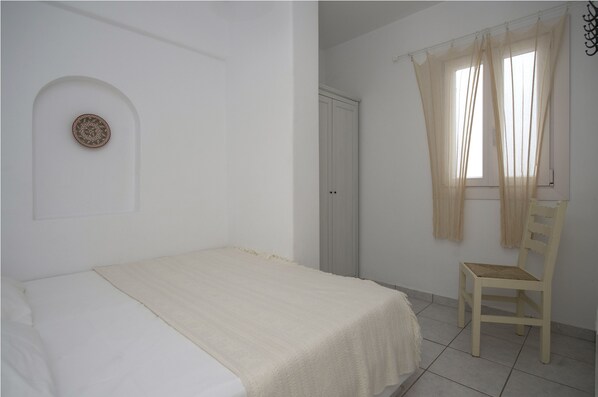 A bedroom with a bed, a chair, a wardrobe, and a window with curtains.