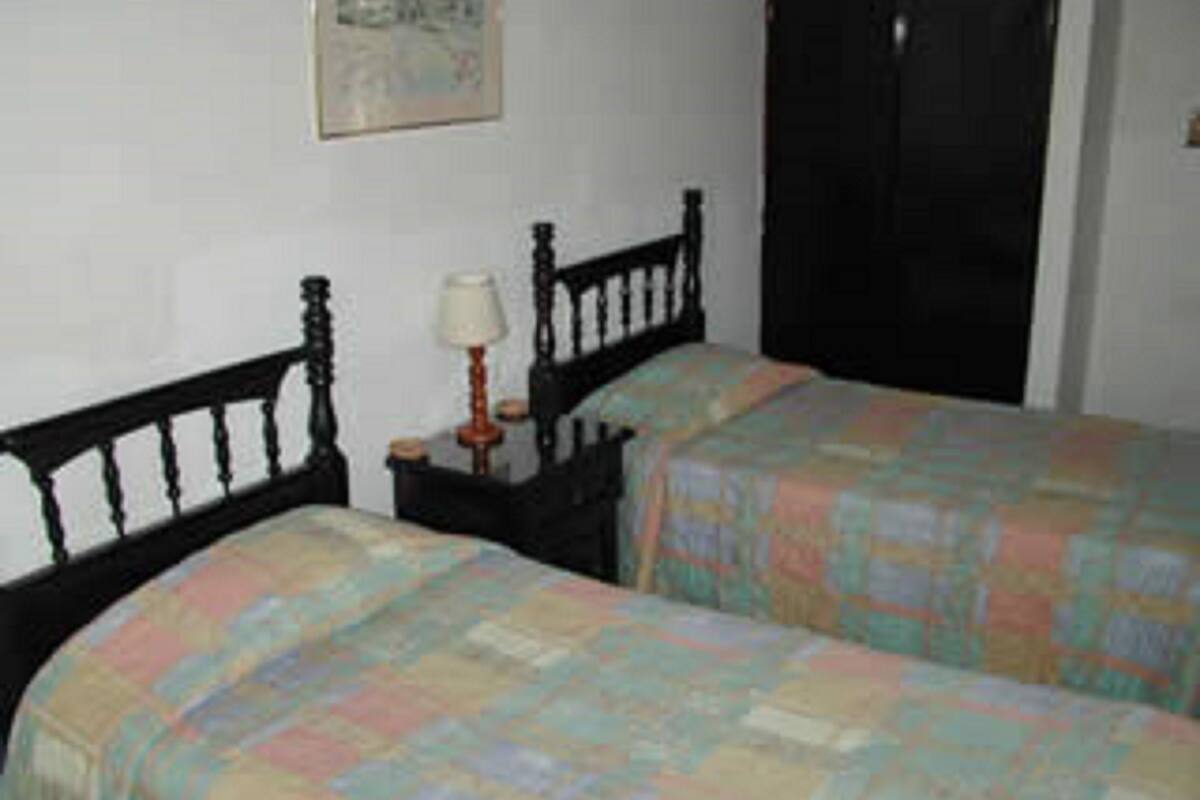 A bedroom with two single beds, a nightstand with a lamp, and a door.