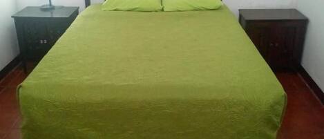 Un lit avec une couvre-lit verte, deux oreillers, une tête de lit en bois et une table de chevet avec une lampe.