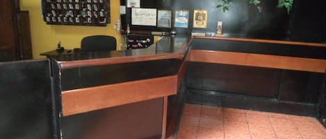 Zona de recepción con un mostrador de madera, un reloj de pared y un tablón de anuncios con varios avisos.
