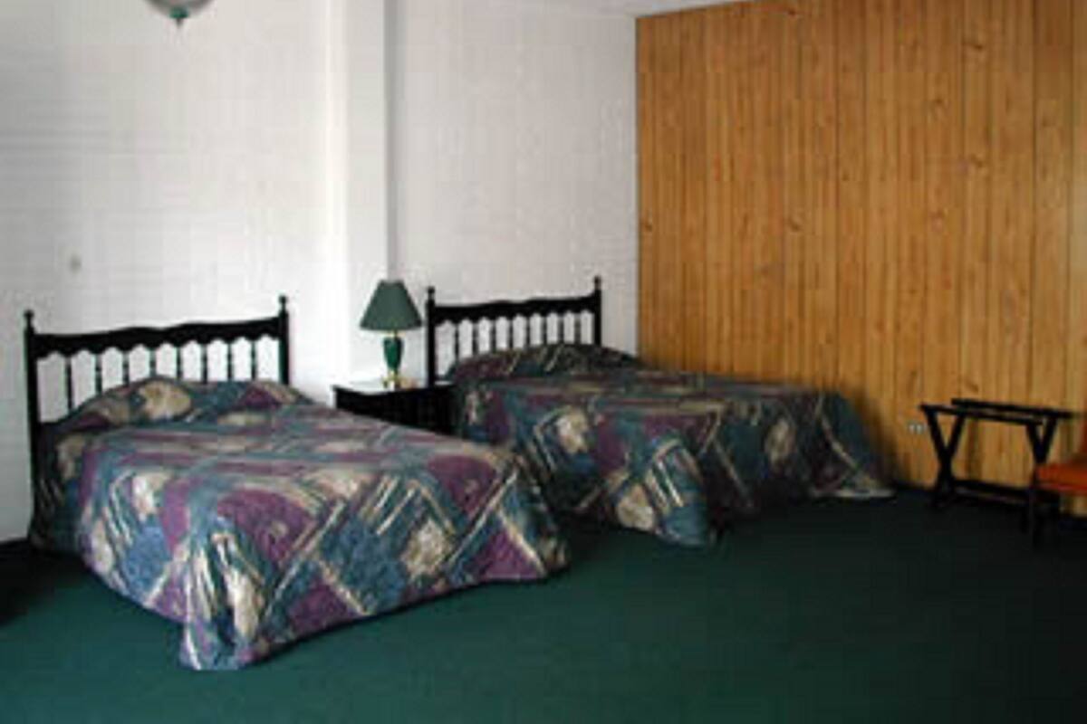 A room with two beds, a wooden wall, and a hanging light fixture.