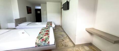 A hotel room with two beds, a ceiling fan, a TV mounted on the wall, and a small wooden shelf.