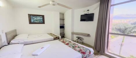 A hotel room with two beds, a ceiling fan, a TV, and a large window with a view.