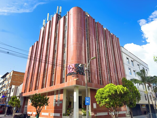 A hotel with a prominent red facade, a central entrance with steps, and a sign indicating it is a hotel.