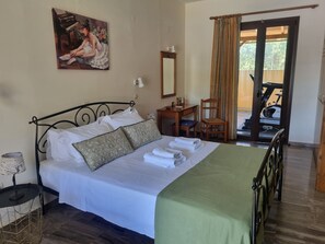 A neatly made bed with pillows, a desk with a chair, a painting on the wall, and a view of an outdoor exercise area.