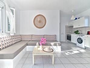 A modern kitchen with a built-in washing machine, a dining area with a table and chairs, and a patterned sofa.