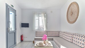 A modern living room with a grey sofa, a small table with a hat, and a TV mounted on the wall. - Poseidon | 2 Bedroom Family Apartment with Sea View and Patio, Cleopatra Homes Paros (Paros)