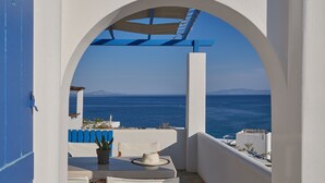 A white outdoor seating area with a table and chairs, a potted plant, and a view of the sea and distant land. - Poseidon | 2 Bedroom Family Apartment with Sea View and Patio, Cleopatra Homes Paros (Paros)