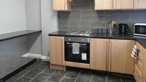 A modern kitchen with wooden cabinets, a black countertop, a stove, an oven, and a microwave. - Encore Rooms (Scunthorpe)