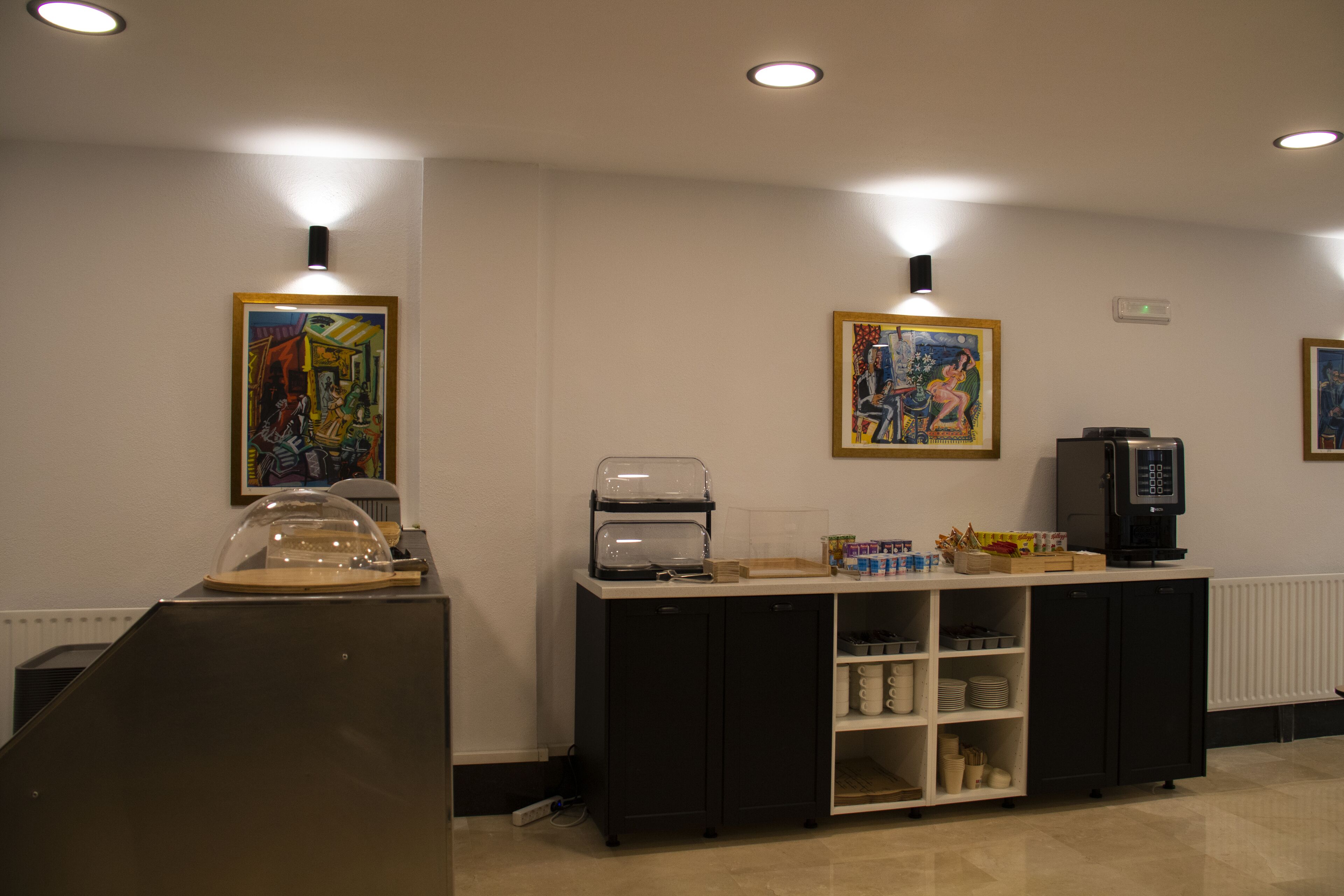 Un área de recepción con mostrador, máquina de café, refrigerador y obras de arte enmarcadas en las paredes.