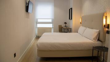 Habitación de hotel con una cama grande, una mesita pequeña, una silla, un televisor montado en la pared y una ventana con vistas al exterior.