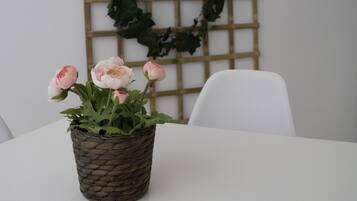 A white table with a woven basket containing pink flowers, a white chair, and a wooden lattice wall with green foliage.
