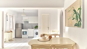 Eine moderne Küche mit weißen Schränken, einem Edelstahlkühlschrank und einer Waschmaschine. Es gibt einen Essbereich mit Tisch und Stühlen, sowie ein Bild an der Wand.