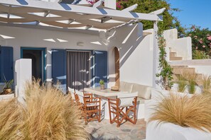 A white building with blue shutters, a patio with wooden chairs, and a pergola.