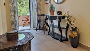 Ein Zimmer mit einem Holzsessel, einem Tisch mit einer dekorativen Vase, einem Spiegel und einem Fenster mit Vorhängen.