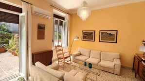 Ein Wohnzimmer mit einem beigen Sofa, einem Holzschaukelstuhl, einem Glastisch und zwei gerahmten Bildern an der Wand.