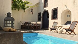 A pool area with a stone bench, wooden chairs, and a table. - Winery Villa. Old winery converted into a stylish traditional villa with pool (Φοινικιά)