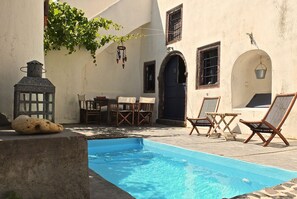 A pool area with a stone bench, wooden chairs, and a table.