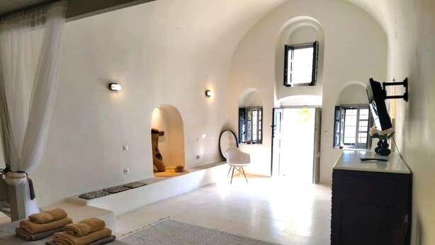 A spacious bedroom with a large bed, a desk, and a chair. There are two windows and a door leading to another room. - Winery Villa. Old winery converted into a stylish traditional villa with pool (Φοινικιά)