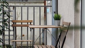 A small outdoor patio area with a wooden table and bench, a potted plant, and a view of a garden. - Temple Apartments (Belgrade)