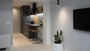 A modern kitchen with a built-in stove, bar stools, and a flat-screen TV mounted on the wall. - Temple Apartments (Belgrade)