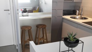 A modern kitchen with white countertops, stainless steel appliances, wooden stools, and a potted plant. - Temple Apartments (Belgrade)