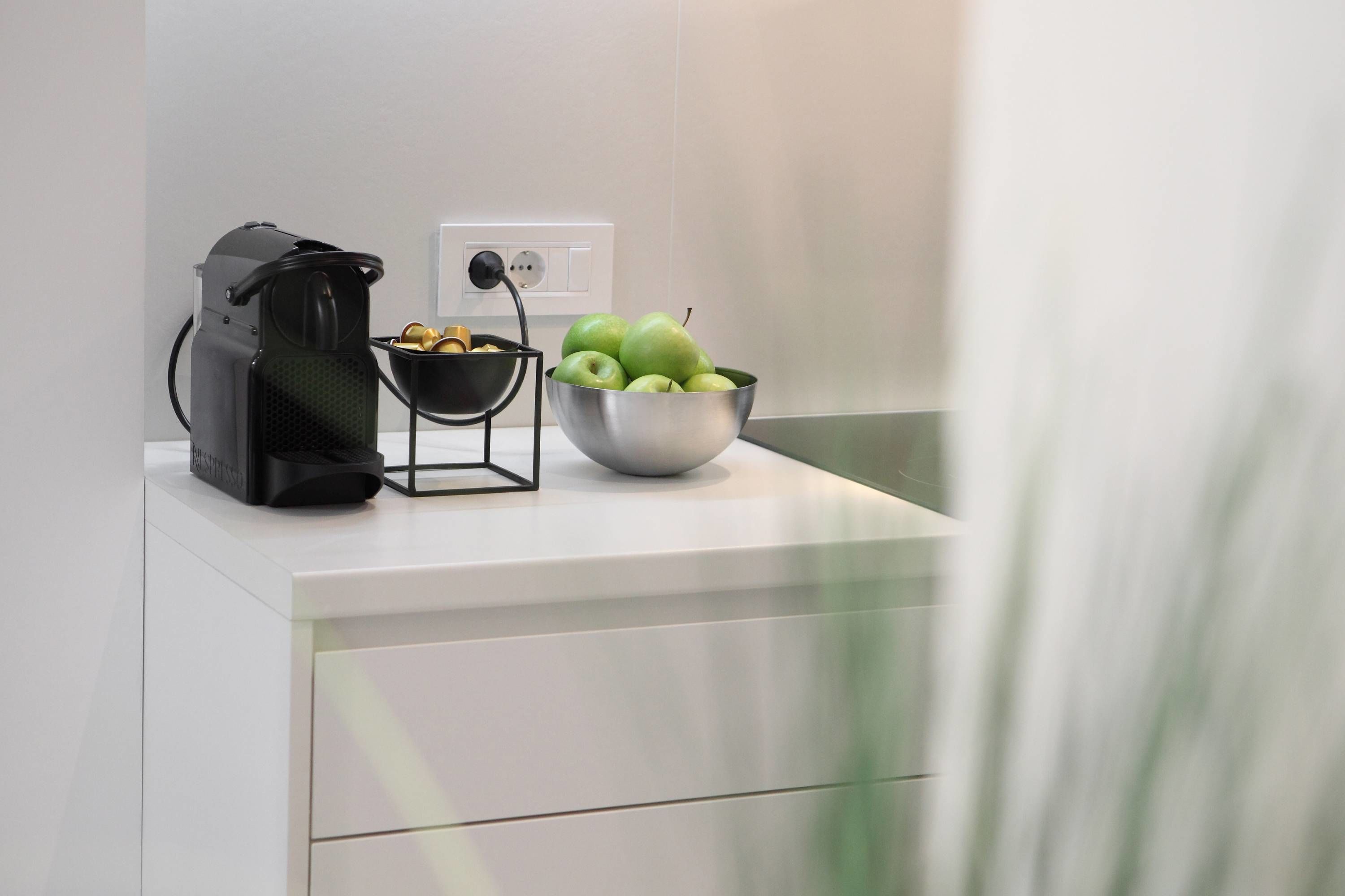 A kitchen counter with a coffee maker, a bowl of fruit, and a power outlet.