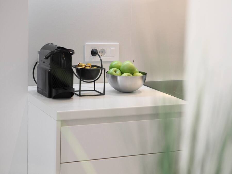 A kitchen counter with a coffee maker, a bowl of fruit, and a power outlet.