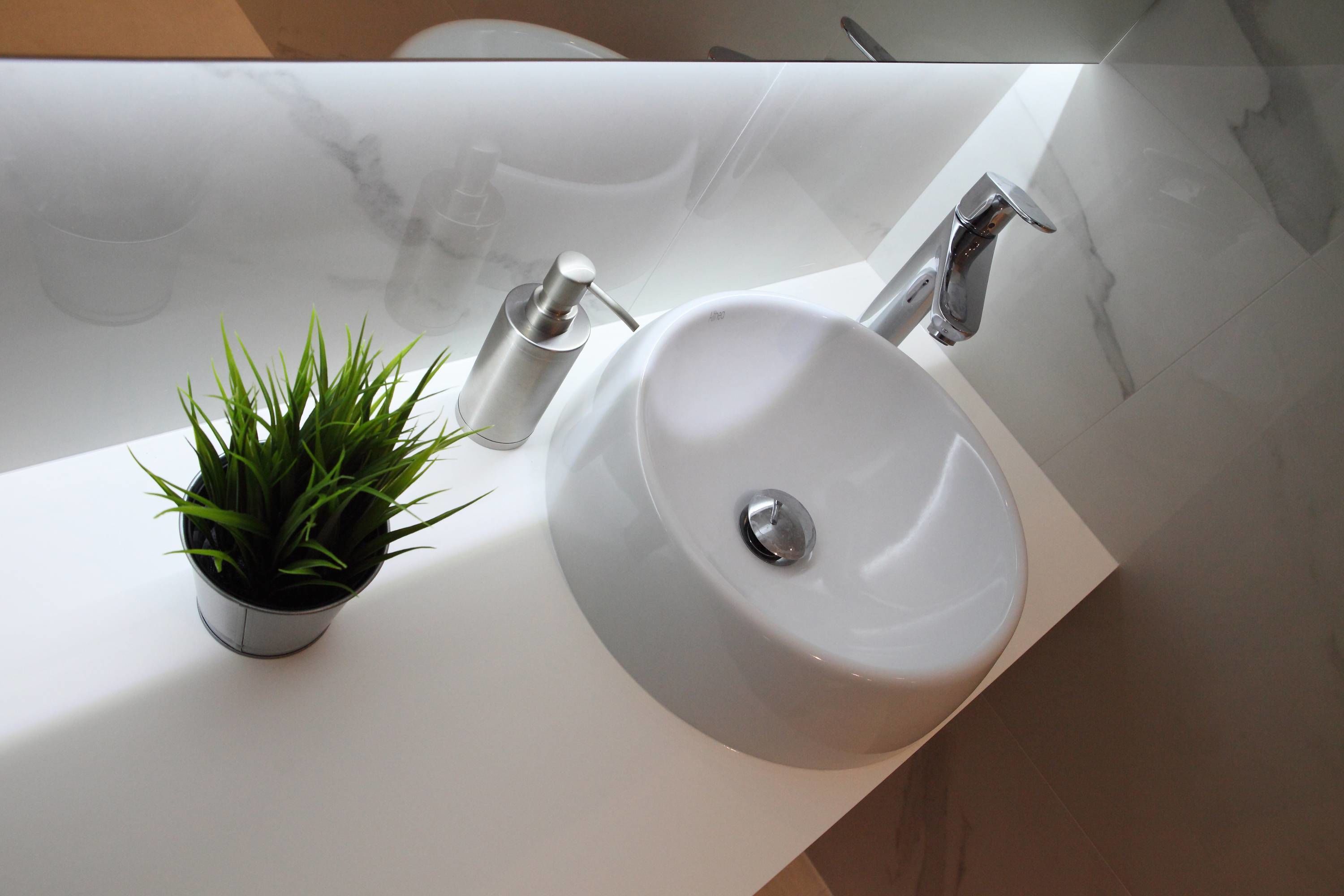 Un bagno con un lavandino bianco, una piccola pianta in vaso e un rubinetto moderno.