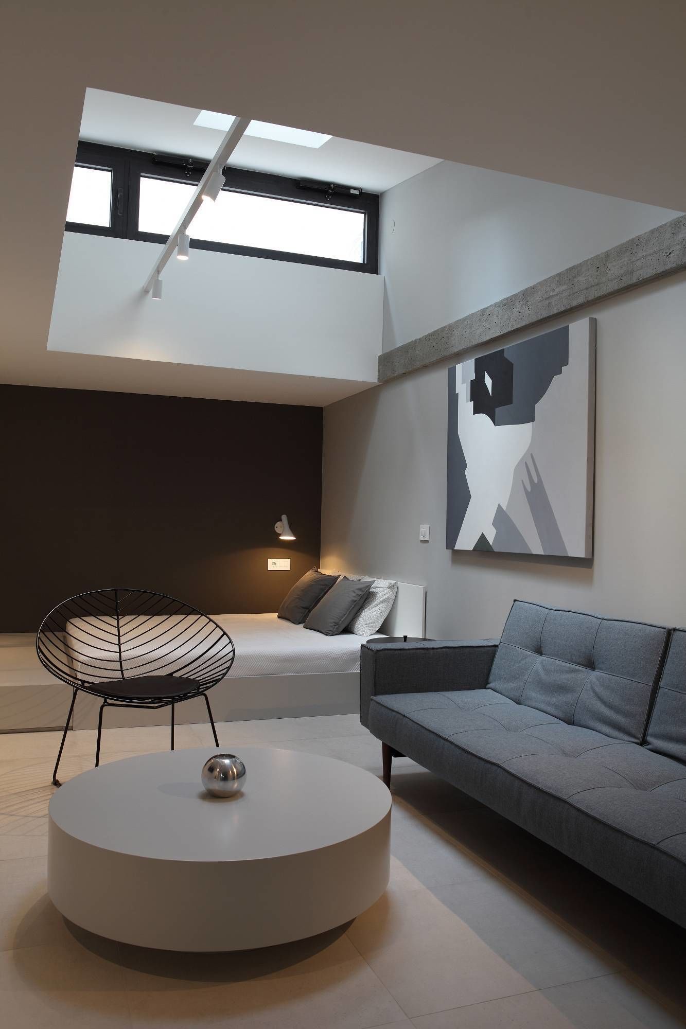 Una sala de estar moderna con tragaluz, una mesa redonda, un sofá y una silla original de estructura metálica.