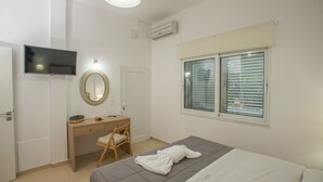 A bedroom with a bed, a desk, a chair, a TV, and a window with blinds. - Kalamaki Riviera Deluxe Apartment (Καλαμάκι)
