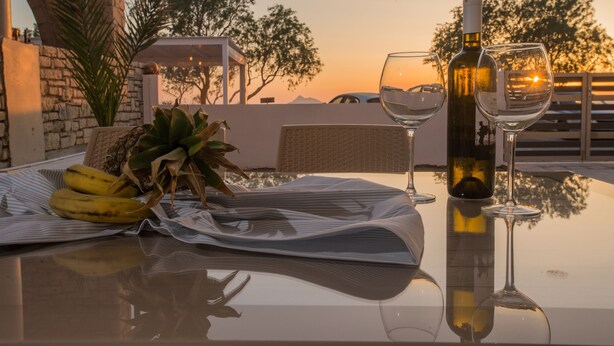 A table with a bottle of wine, two wine glasses, and a plate of bananas. - Kalamaki Riviera Deluxe Apartment (Καλαμάκι)