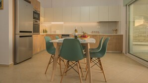 A modern kitchen with a dining table, chairs, and a refrigerator. - Kalamaki Riviera Deluxe Apartment (Καλαμάκι)