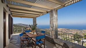 Una terraza con mesa y sillas, una planta de cactus y vistas al mar y al paisaje.