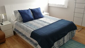A neatly arranged bedroom with a patterned bedspread, two pillows, a bedside table with a lamp, and a floor lamp. - Barrañan Beach Apartments, Apartment 12 (Arteixo)