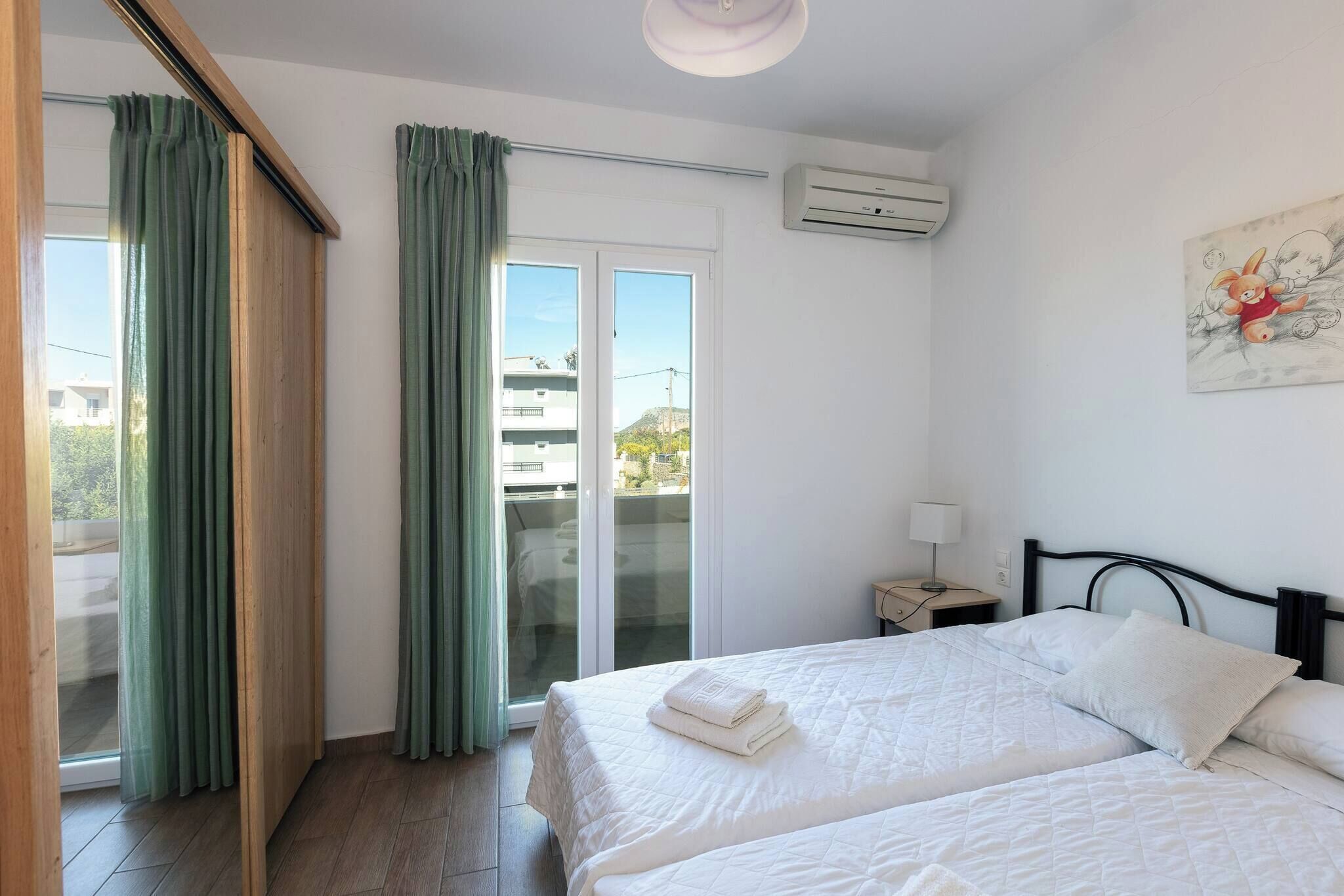 A hotel room with two beds, a sliding glass door to the balcony, a ceiling fan, and a wall-mounted air conditioner.