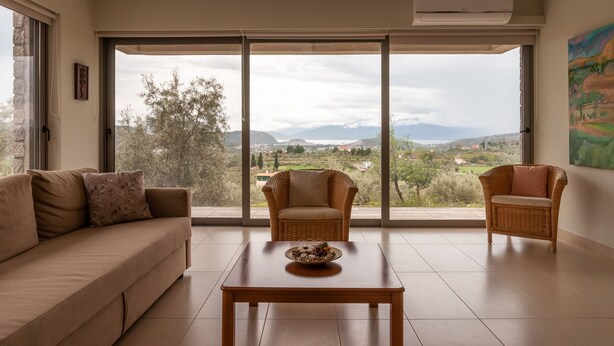 Ein Wohnzimmer mit einer Couch, zwei Korbstühlen, einem Couchtisch und einem großen Fenster mit Blick auf eine Landschaft.