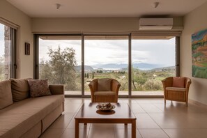 A living room with a sofa, two wicker chairs, a coffee table, and a large window offering a view of a landscape.