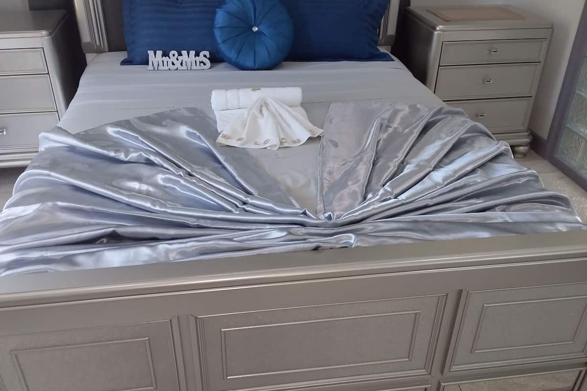 A bed with a metallic, shiny cover, a blue pillow, and a sign that reads "Mr & Mrs".