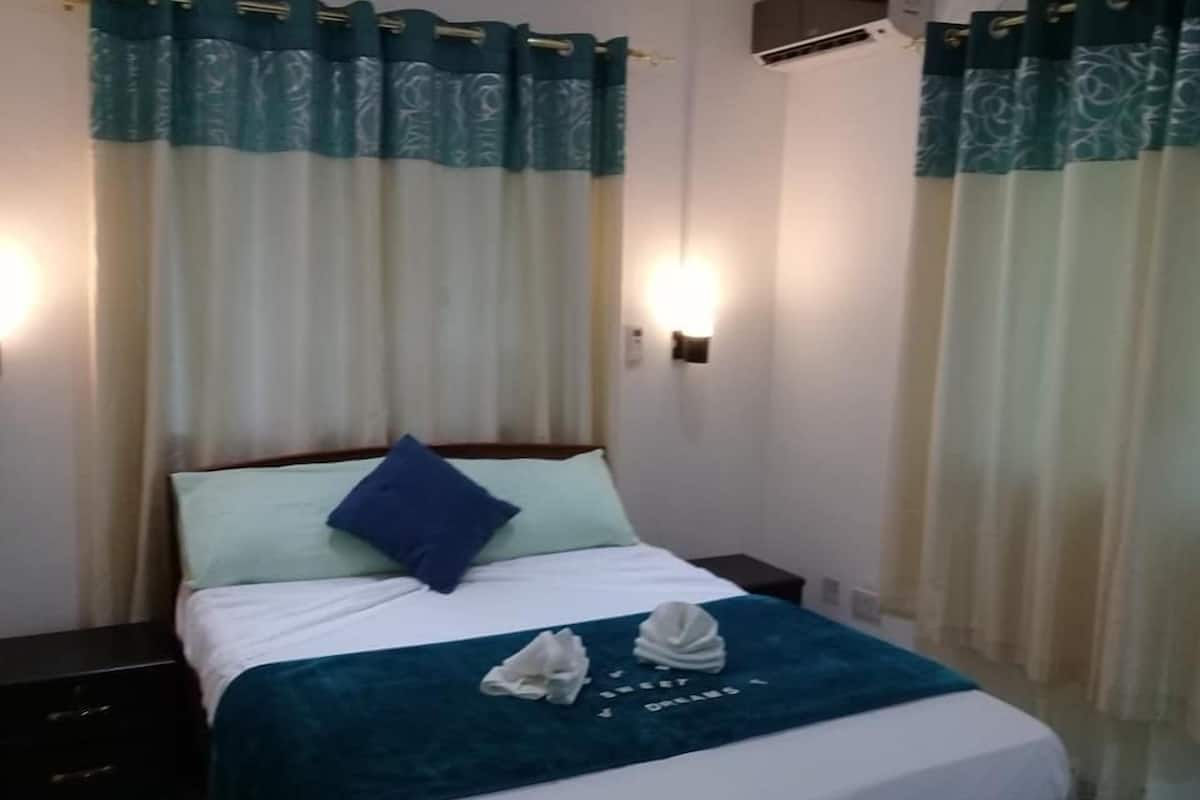 A hotel room with a bed, a nightstand, a wall-mounted air conditioner, and curtains.
