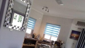 Una sala de estar moderna con un sofá, una mesa de centro y un espejo grande. Hay una zona de cocina con ventana y un fregadero.