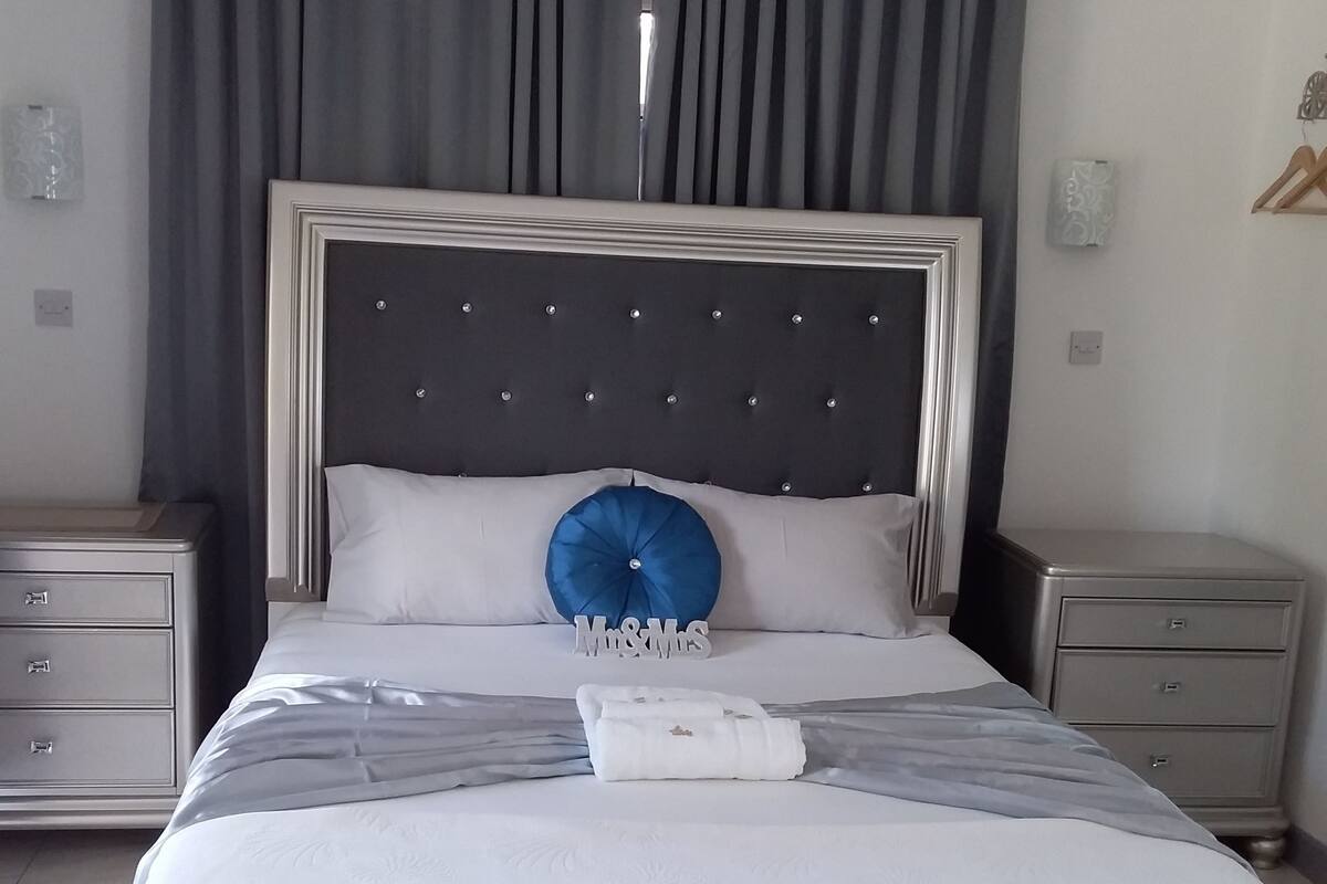 A neatly made bed with a tufted headboard, a blue accent pillow, and a white towel.