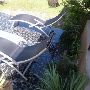 A patio area with a black outdoor table and chairs, a blue tiled floor, and green plants.