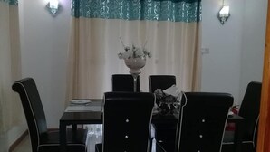 Un comedor con una mesa y sillas, un jarrón con flores y una cortina estampada.