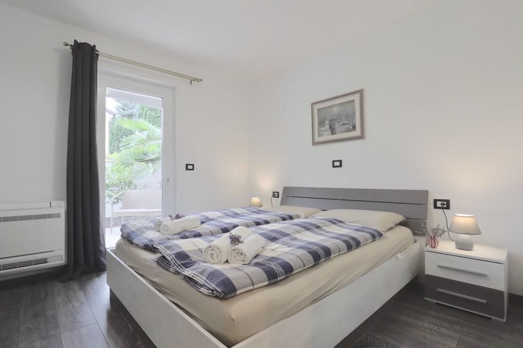 Een slaapkamer met een bed, nachtkastjes, een raam met gordijnen en een ingelijste foto aan de muur.